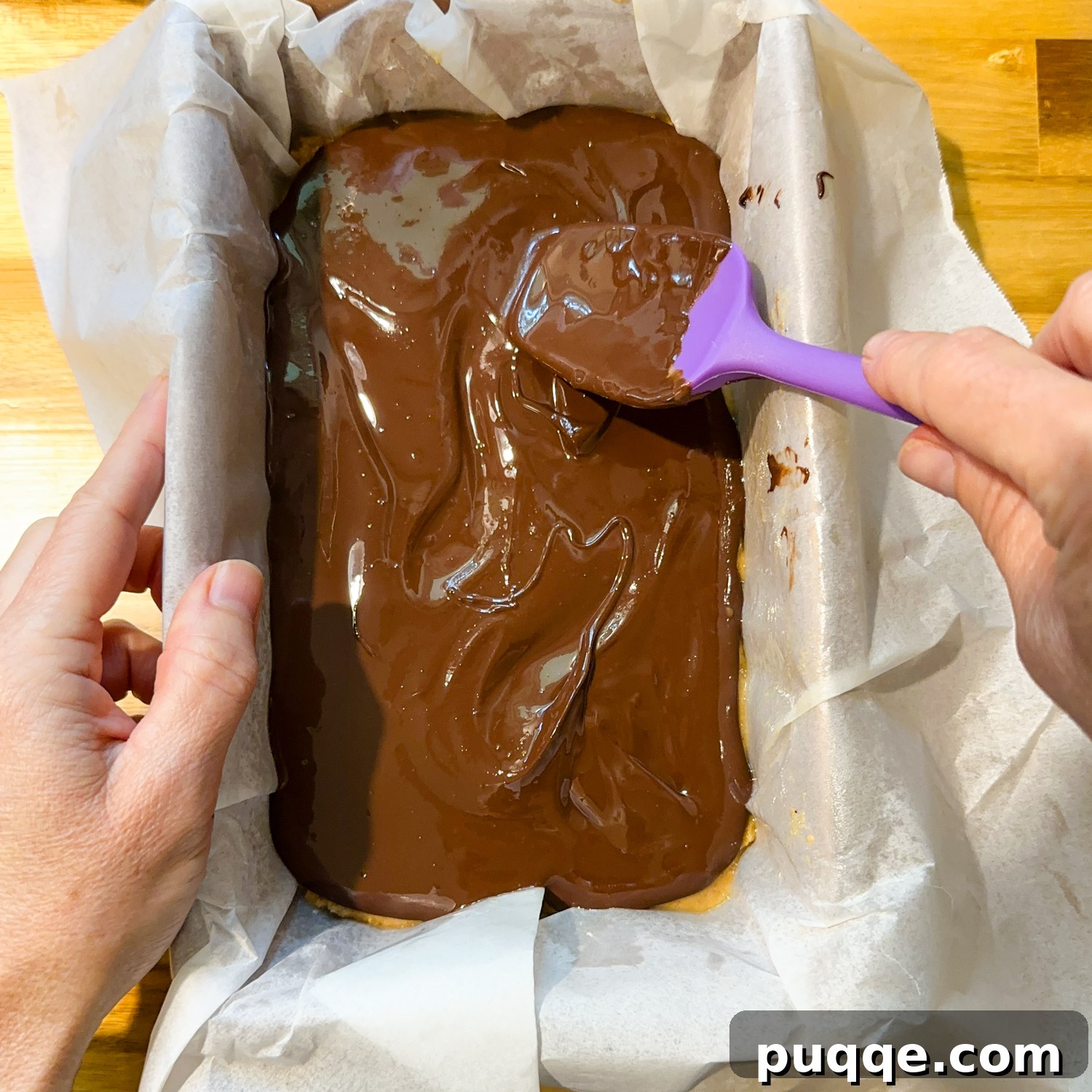 Melty dark chocolate and peanut butter topping being spread over the chilled peanut butter bar mixture.