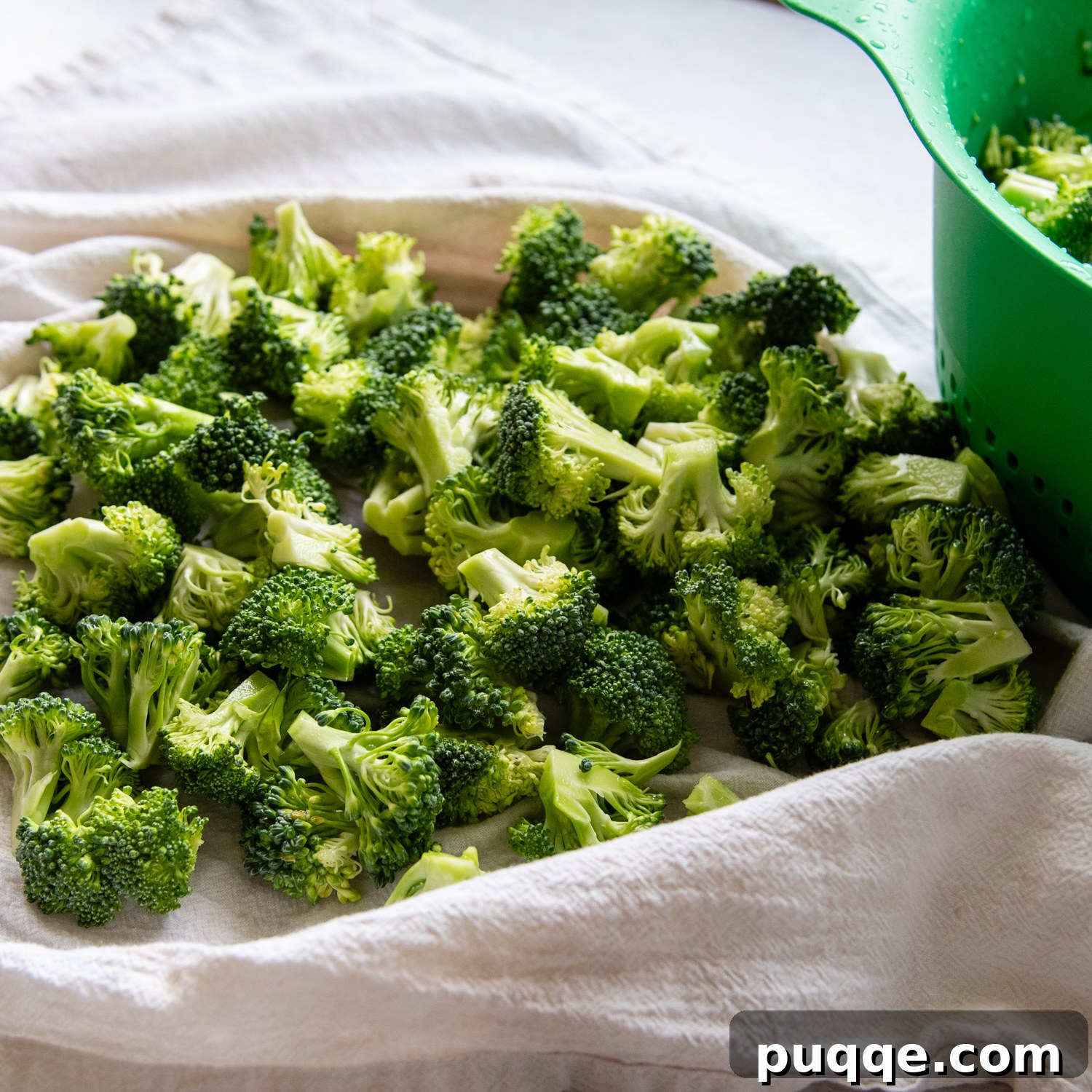 Freshly chopped broccoli florets spread out on a white lint-free dish towel, a crucial step to absorb excess water before mixing into the salad.