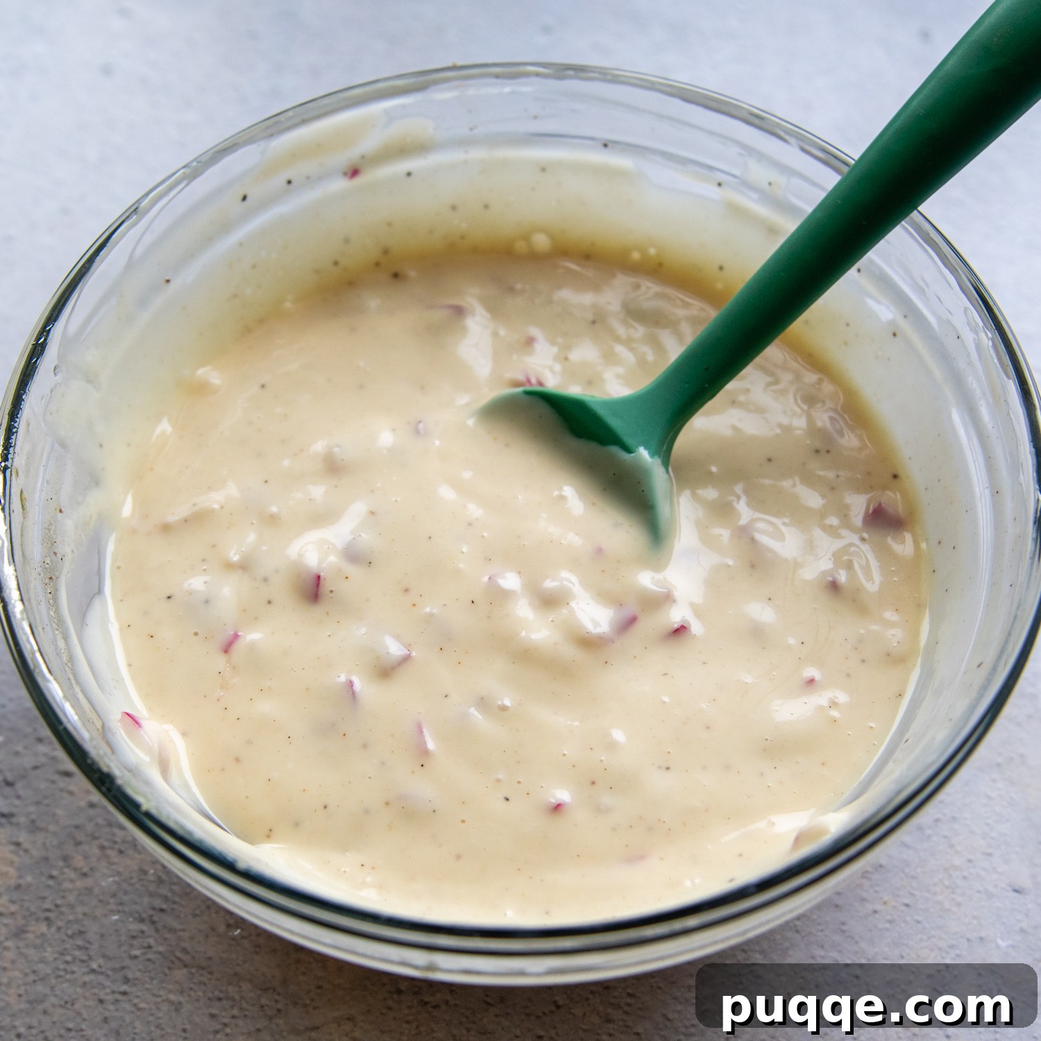 A vibrant, creamy salad dressing in a glass bowl, with a green spoon, ready to be poured over the prepared broccoli salad.