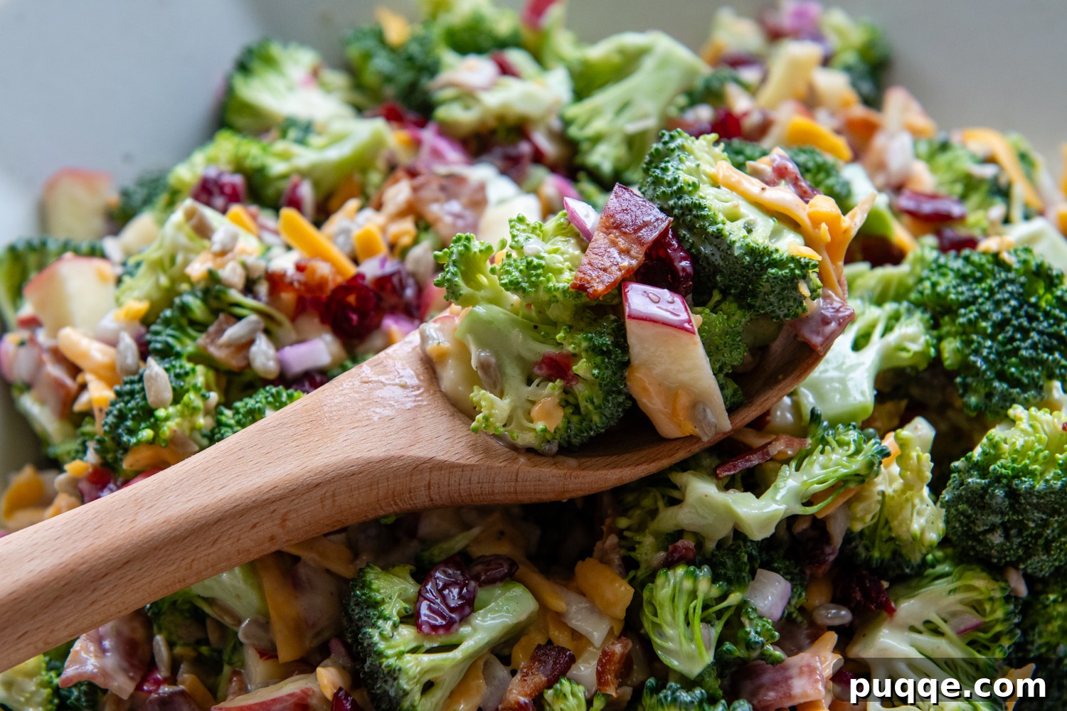 A wooden spoon lifting a generous scoop of the vibrant broccoli salad from a large bowl, showcasing its diverse ingredients.