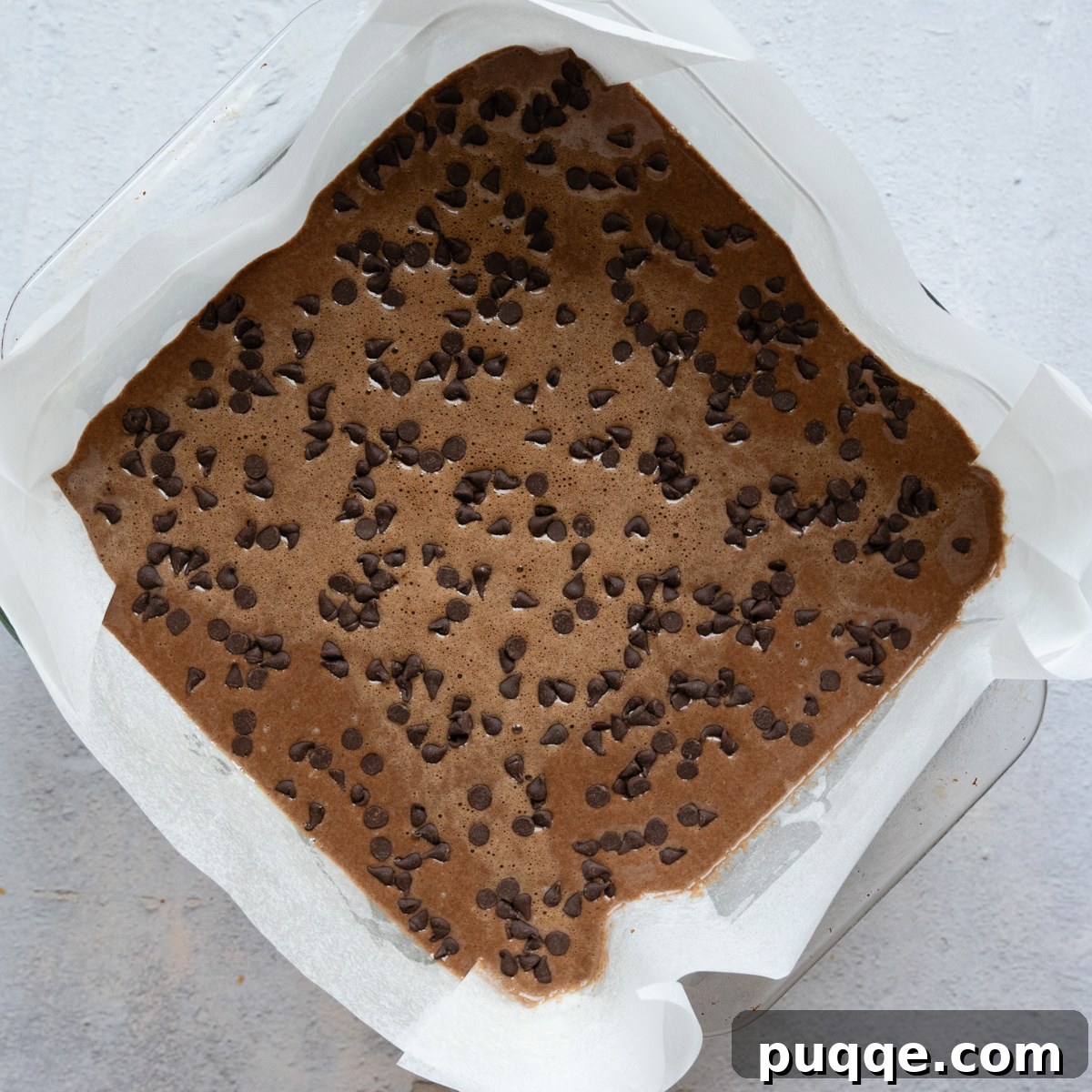 Cake batter poured into a greased 8-inch square baking dish, with chocolate chips sprinkled on top.