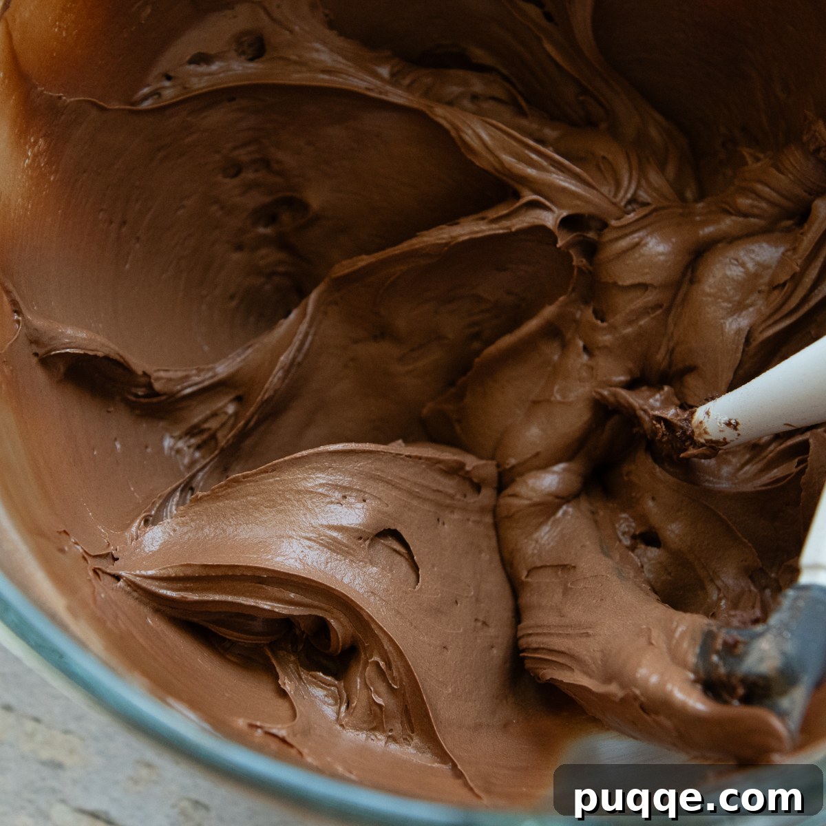 Smooth, rich chocolate frosting in a glass bowl with a white spatula.