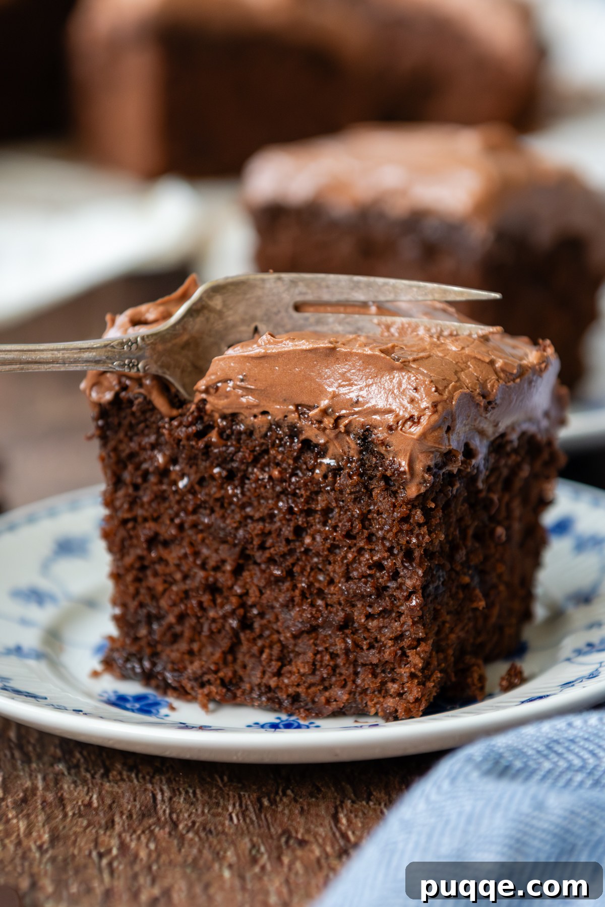 A slice of cake sitting on a glass plate being cut into by a fork, showcasing its moist texture.