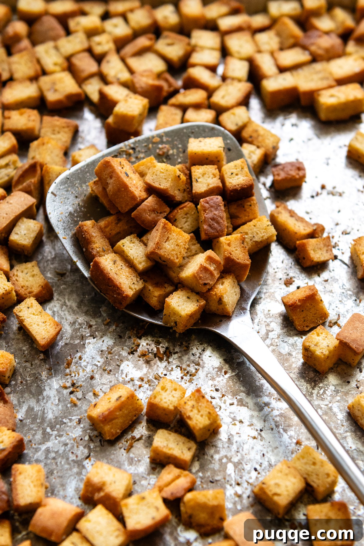Metal spoon resting on a baking pan filled with golden-brown, cooked gluten-free croutons.