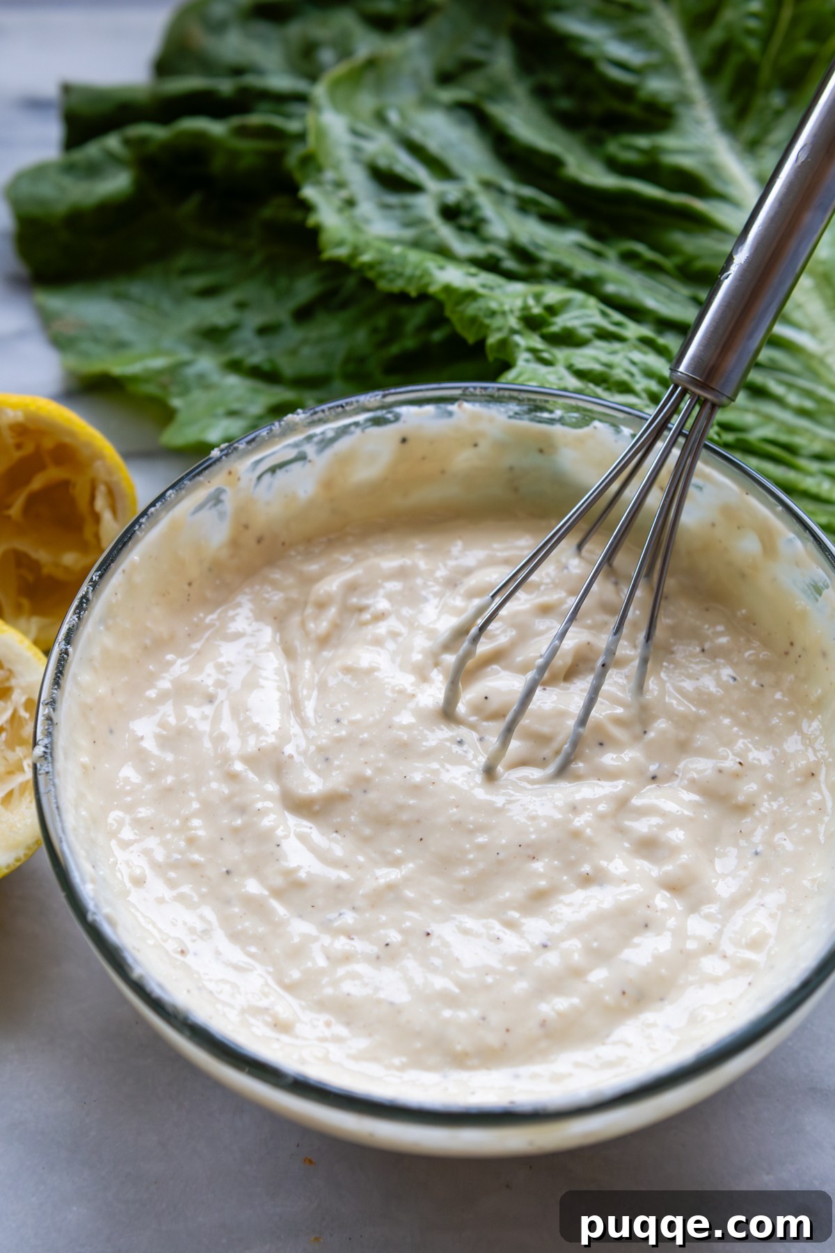 A bowl of rich, creamy Caesar salad dressing with a whisk resting inside.