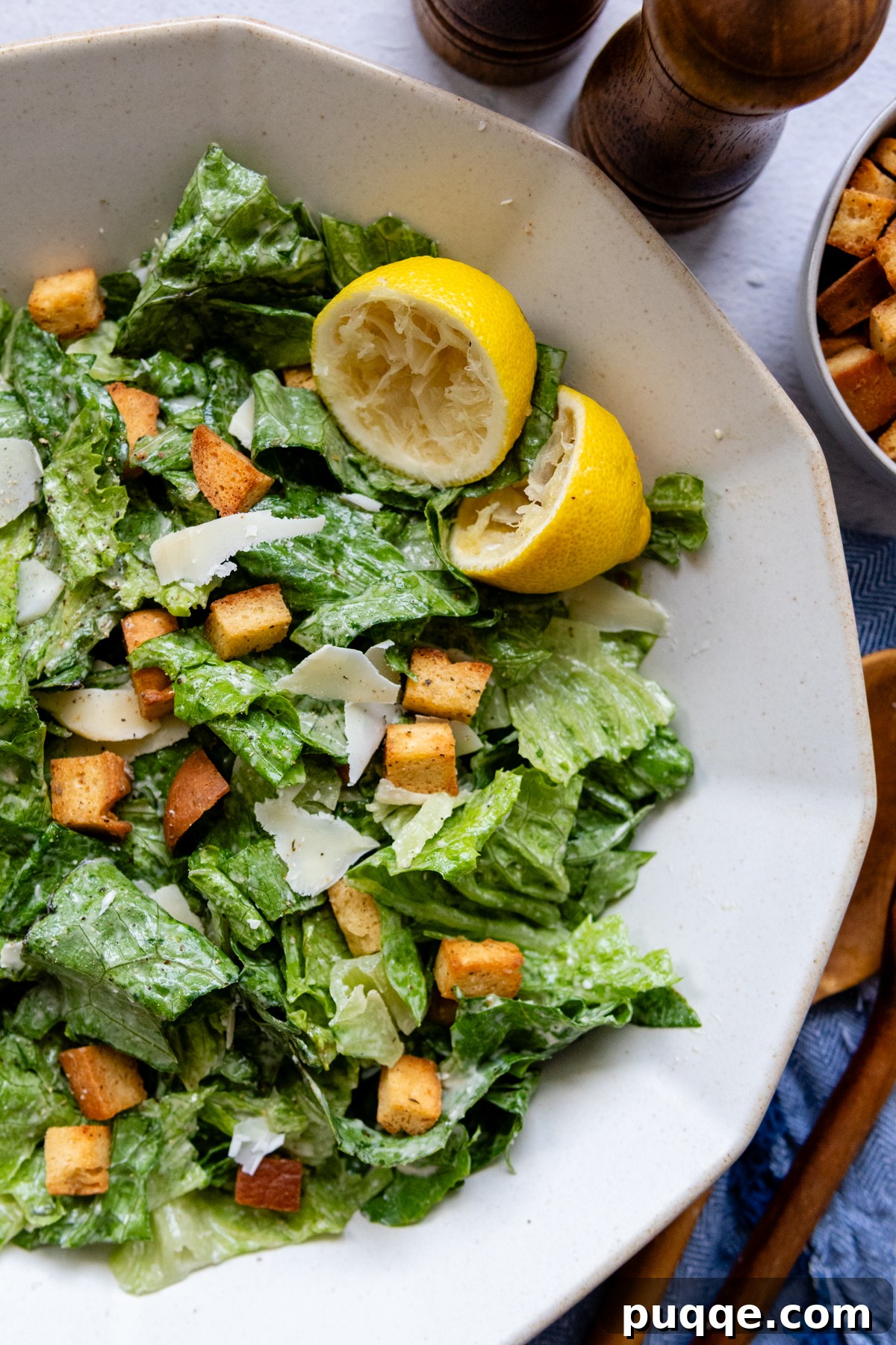 A beautifully presented Caesar salad in a white bowl, garnished with lemon wedges.