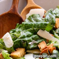 Close up of bowl of Caesar salad with wooden spoons.