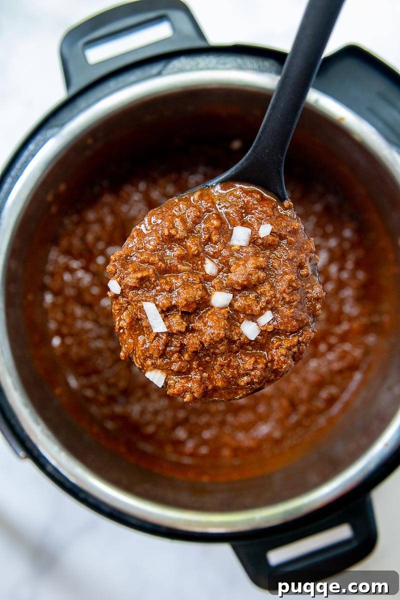 Ultimate Cincinnati Chili 4 A ladle lifts a serving of Cincinnati Chili from an Instant Pot, showcasing its rich texture.