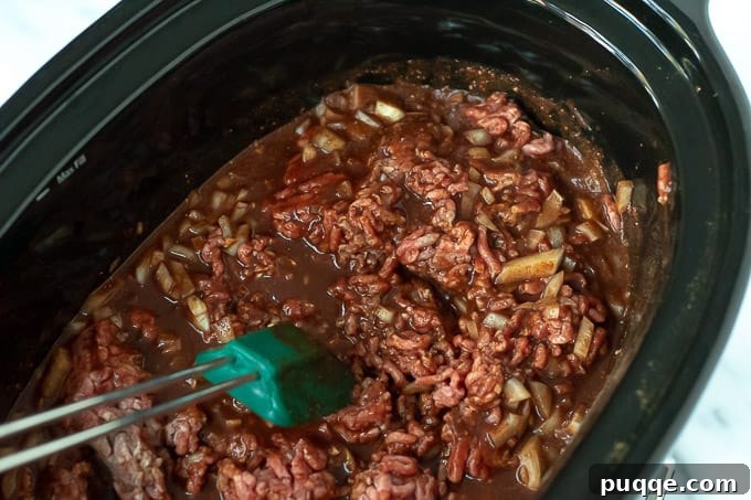 Ultimate Cincinnati Chili 5 Cincinnati Chili being stirred in a slow cooker, highlighting its rich, saucy consistency.
