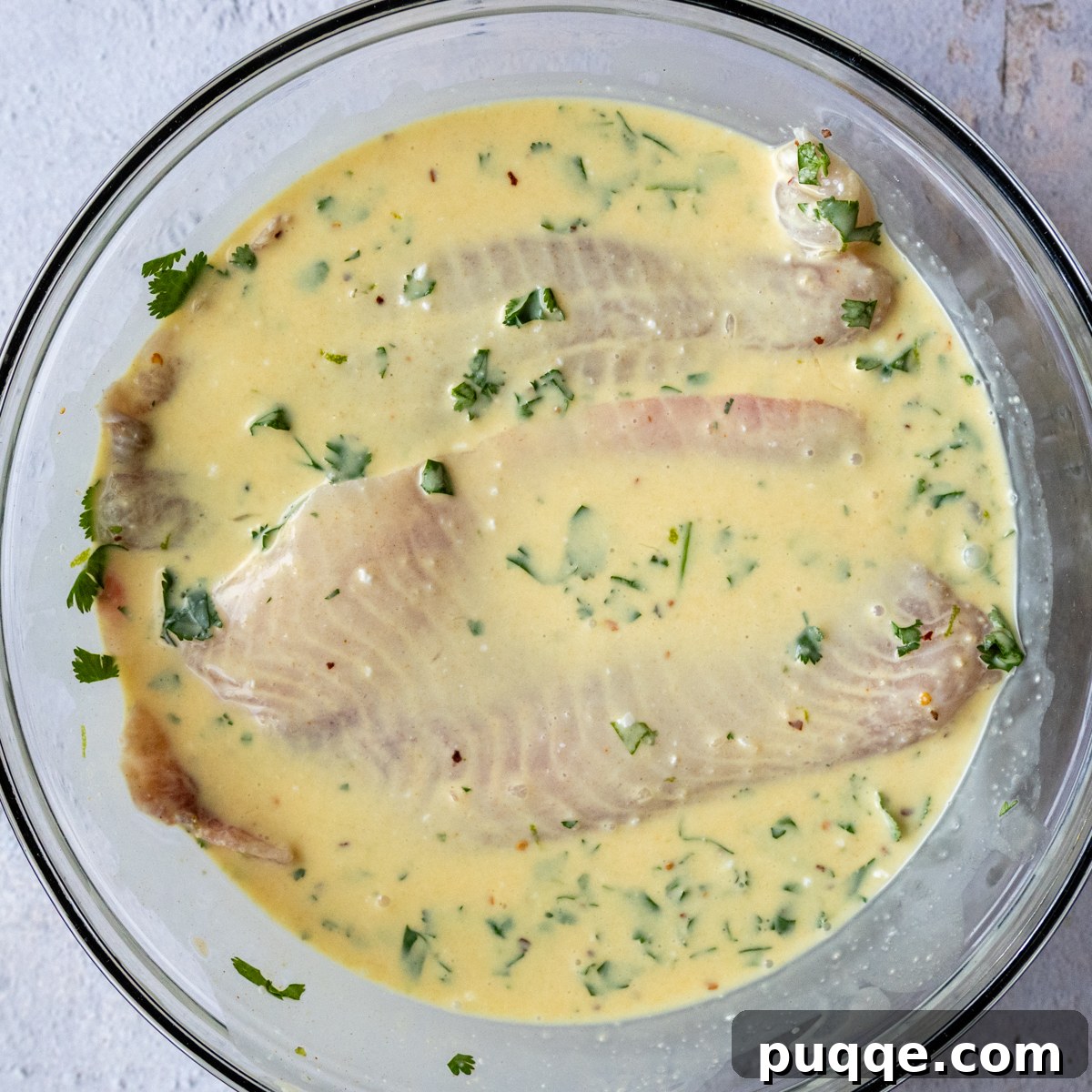 White fish fillets marinating in a creamy coconut sauce in a glass bowl.