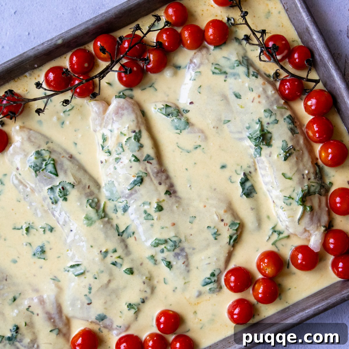 Marinated fish and pre-baked tomatoes on a baking sheet, ready for final baking.
