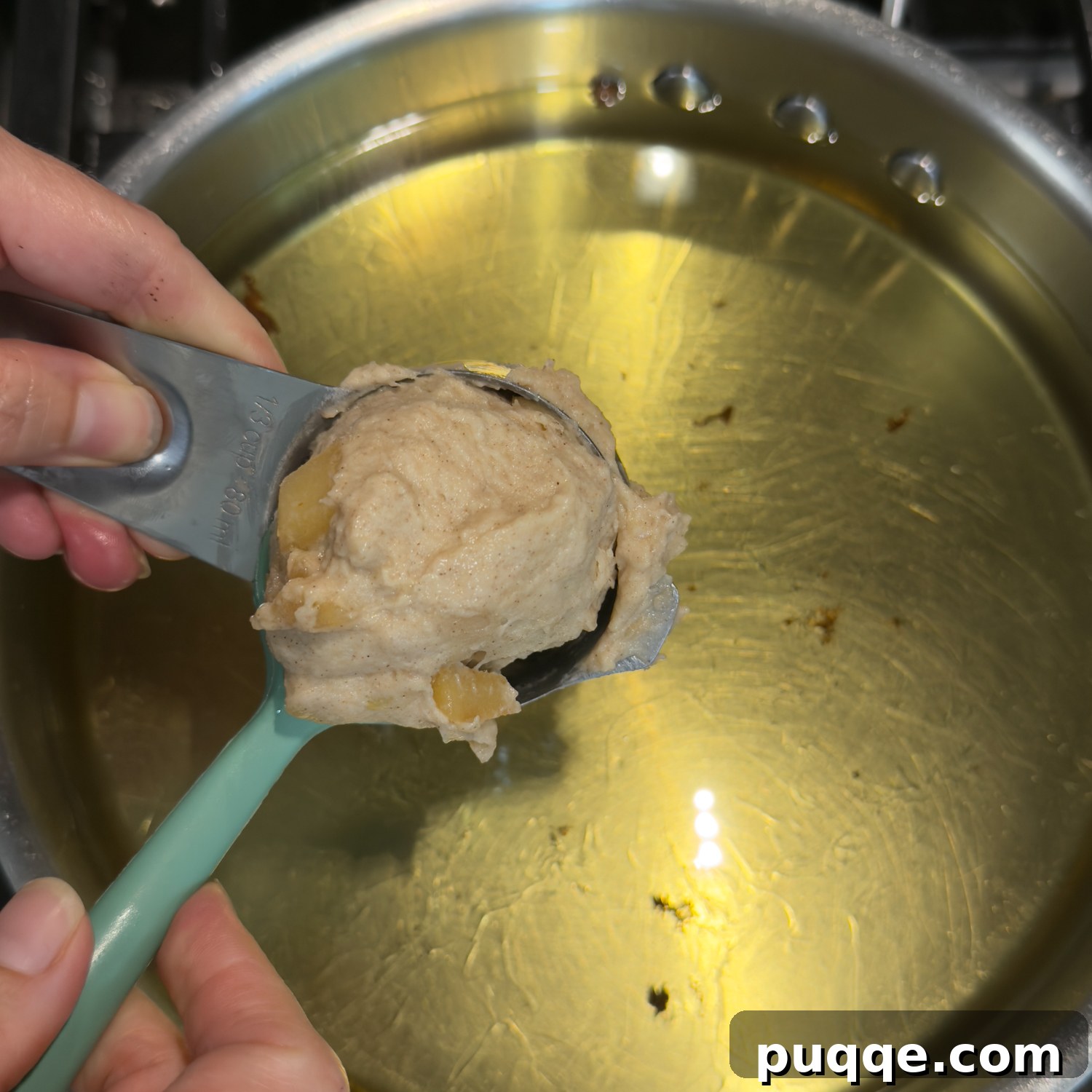 No-Fuss Gluten-Free Apple Fritters 6 A measuring cup holding a doughy fritter over pot of oil.