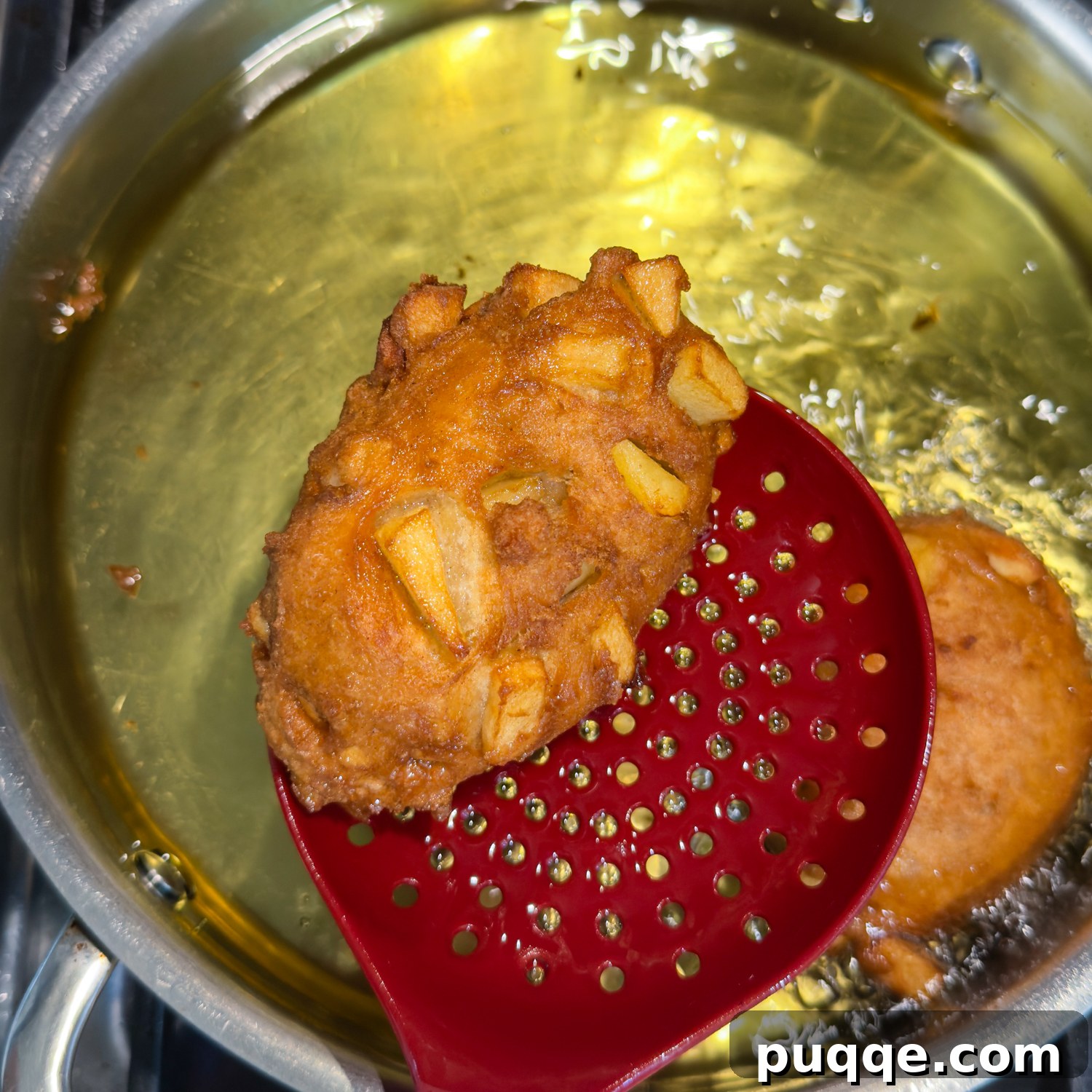 No-Fuss Gluten-Free Apple Fritters 8 Fritter frying with a red slotted spatula.