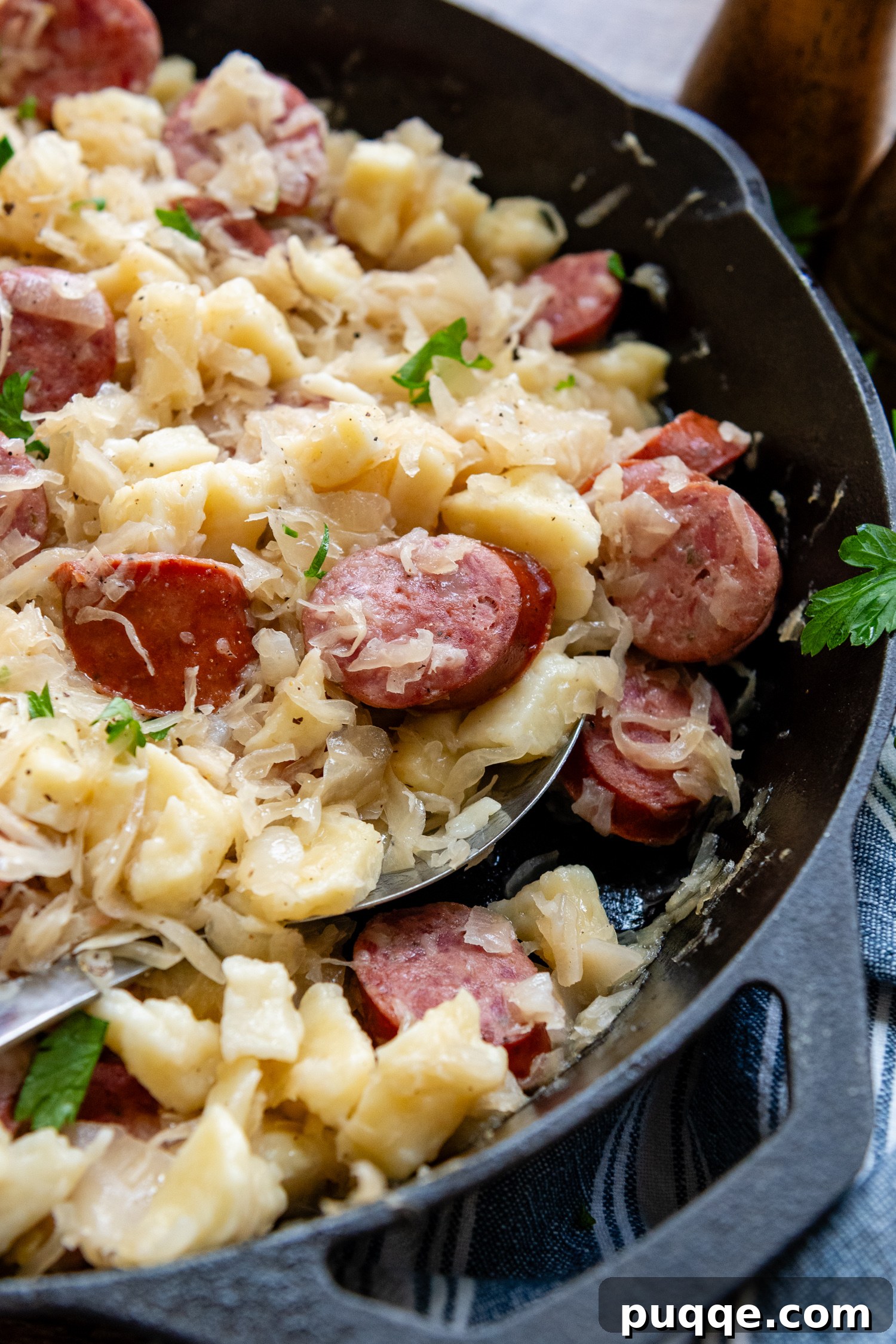 Hearty Gluten-Free German Dumplings and Sausage 9 A close-up of gluten-free dumplings and sausage mixed with sauerkraut in a cast iron skillet with a serving spoon.