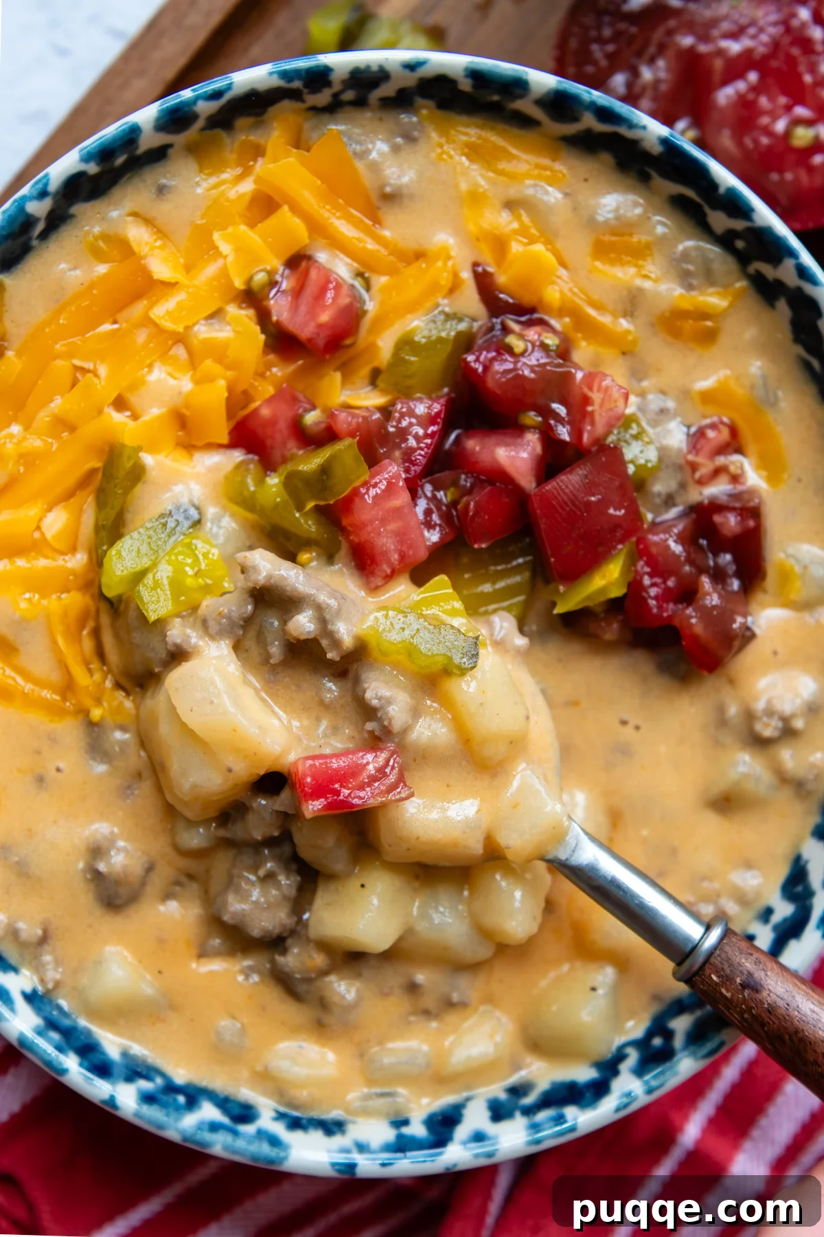 A bowl of thick and creamy gluten-free cheeseburger soup, garnished with fresh toppings, viewed from overhead with a spoon resting in it.