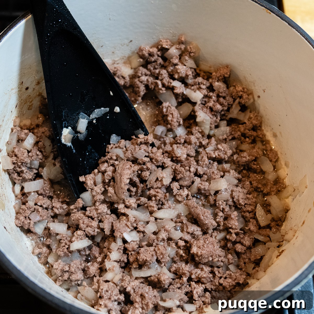 Cooked ground beef and onions in a bowl with a black spoon.