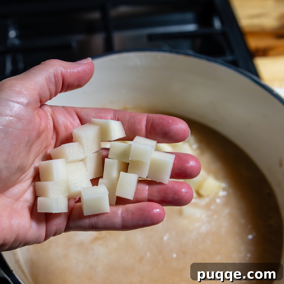 A hand holding a diced potato piece, demonstrating the ideal ¼-inch size for even cooking.
