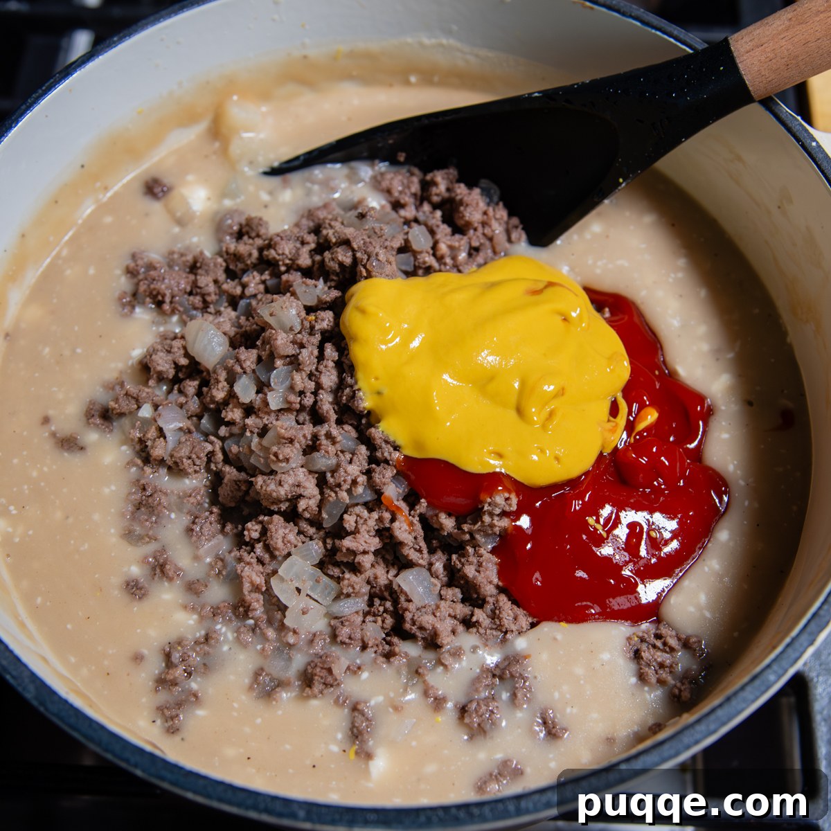 A black spoon mixing cream cheese and cooked ground beef into the soup base.