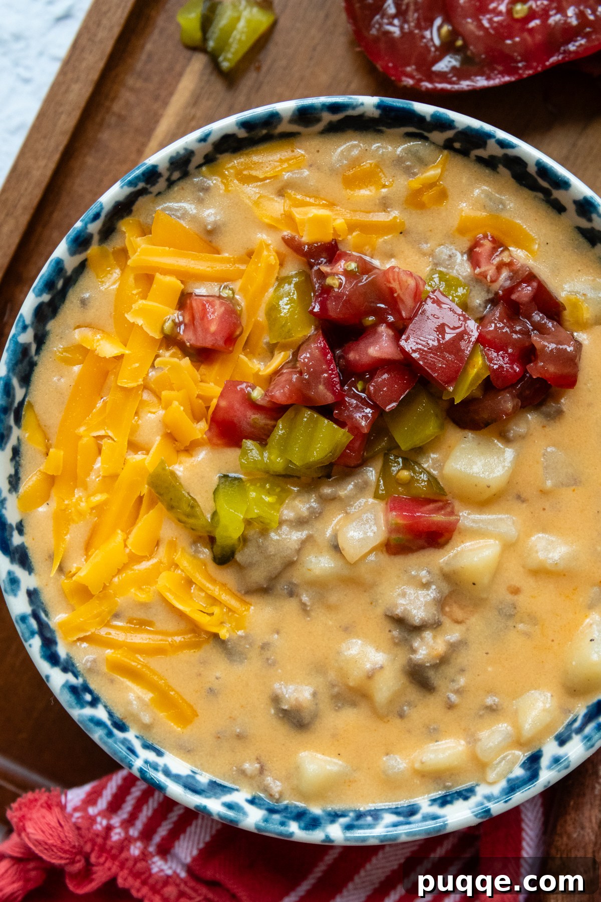 Overhead shot of gluten-free cheeseburger soup in a bowl, generously topped with various burger toppings like relish and diced tomatoes.