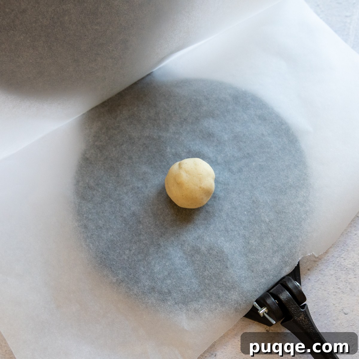 Tortilla ball on top of parchment paper inside a pres.