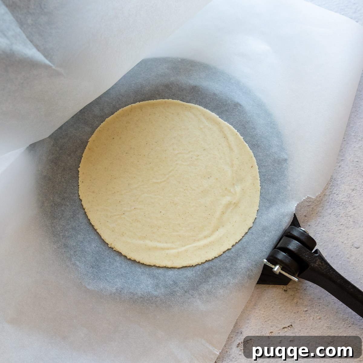 Flattened tortilla on parchment paper on comal.