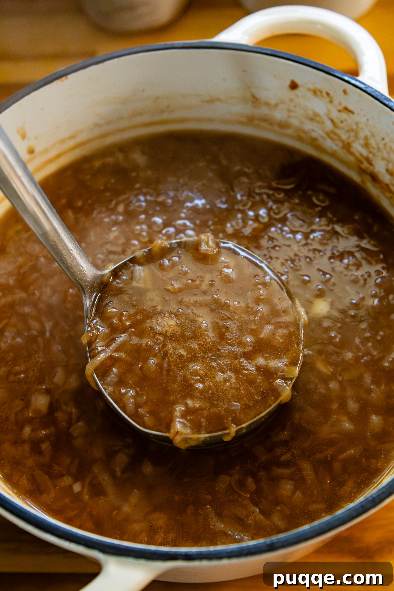 Easy Gourmet Gluten-Free French Onion Soup 11 A ladle filled with rich, savory French onion soup hovering over a large pot brimming with the golden-brown broth and caramelized onions.