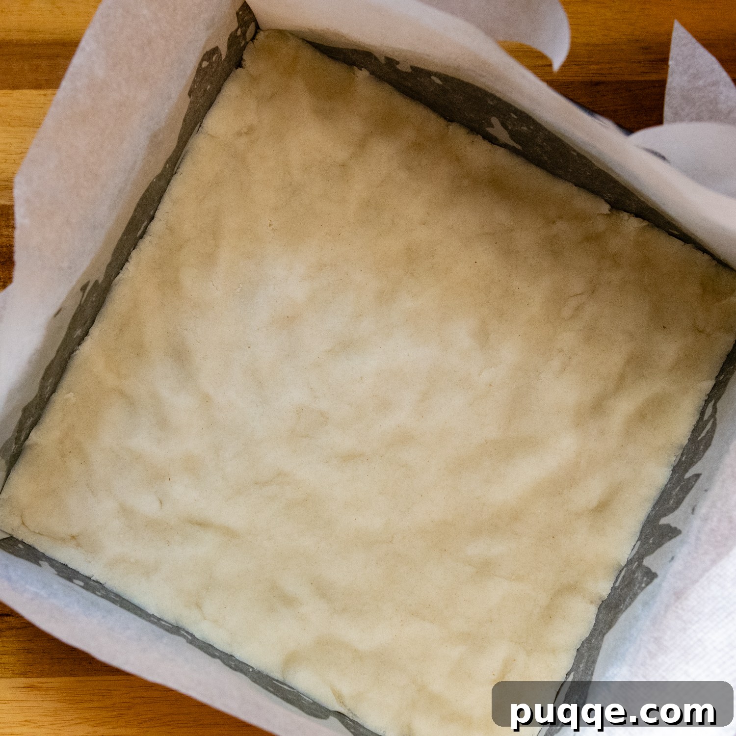 Gluten-free shortbread dough pressed evenly into a prepared baking pan lined with parchment paper.