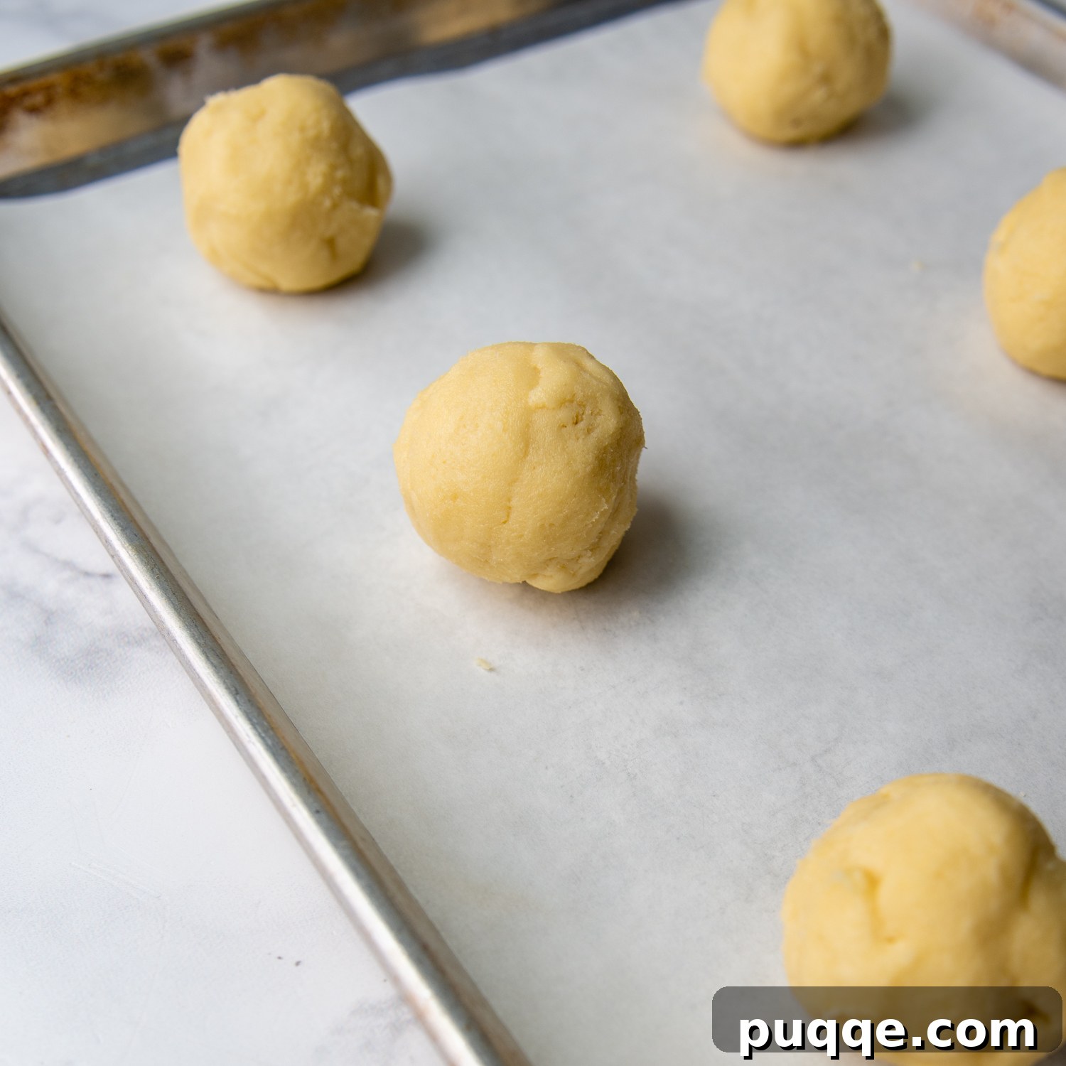 Evenly spaced, formed cookie dough balls resting on parchment paper on a baking sheet, ready for the oven.