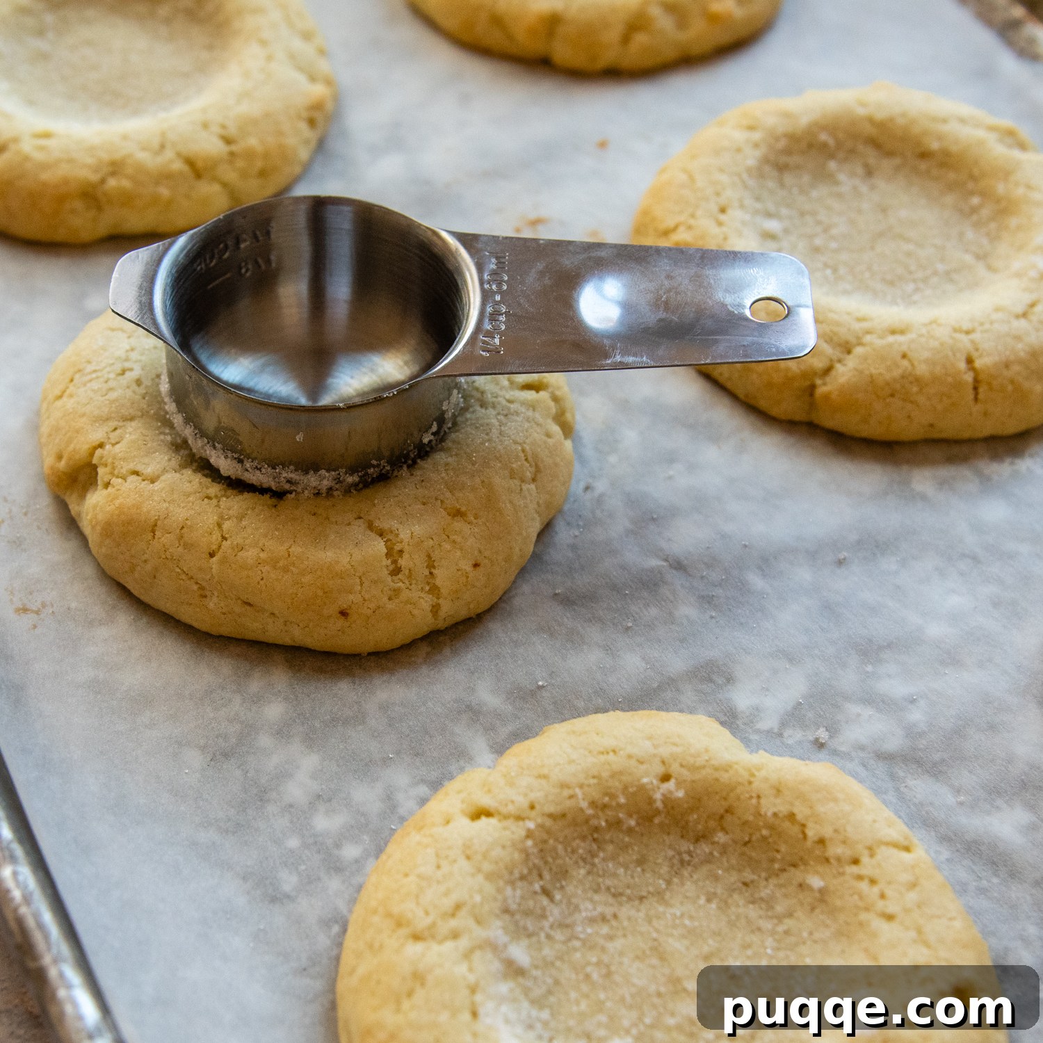 A measuring cup being pressed into the center of a cooled cookie, creating a perfect indentation for the frosting.