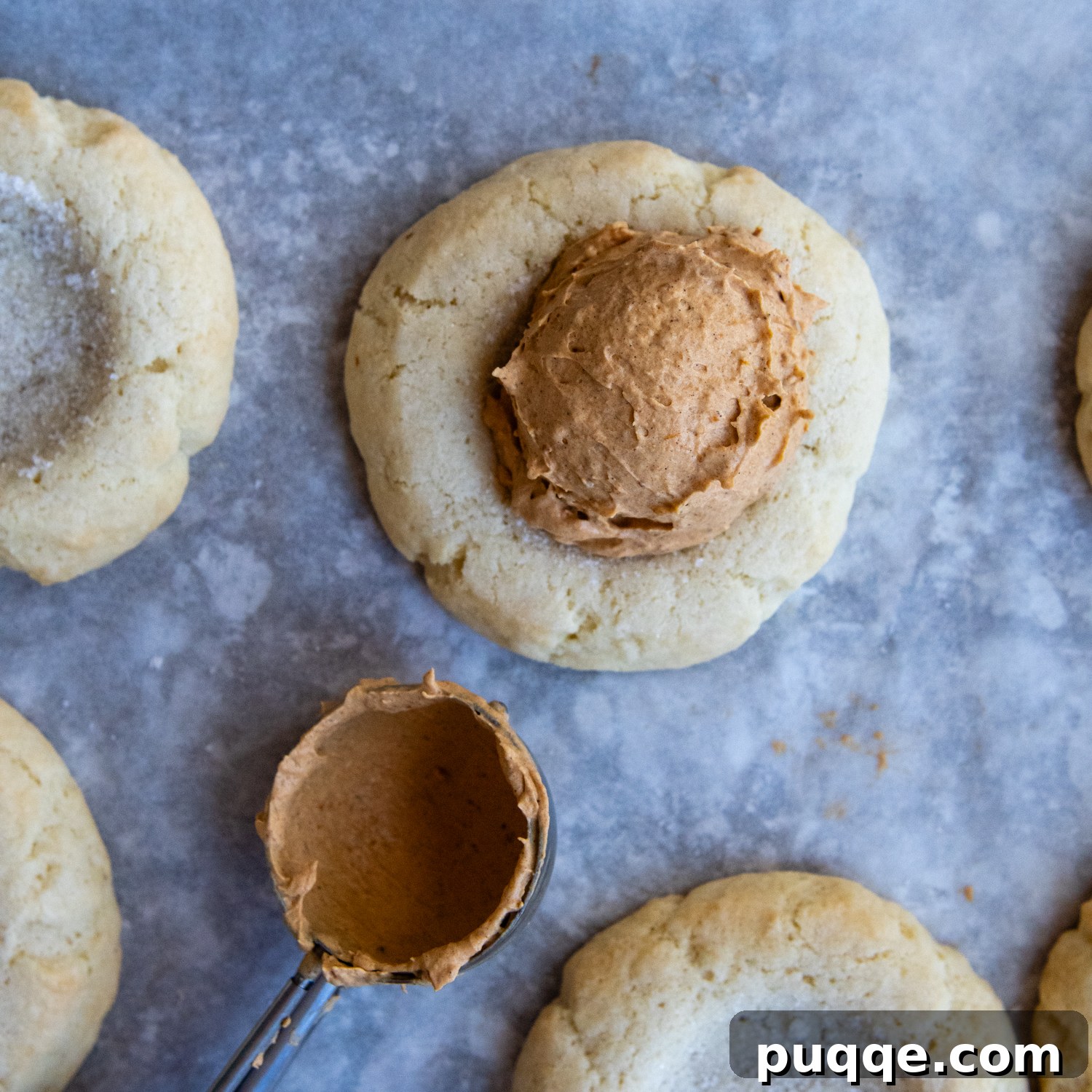 A generous swirl of fluffy pumpkin cream frosting being added to the center of a cooled cookie, completing the dessert.