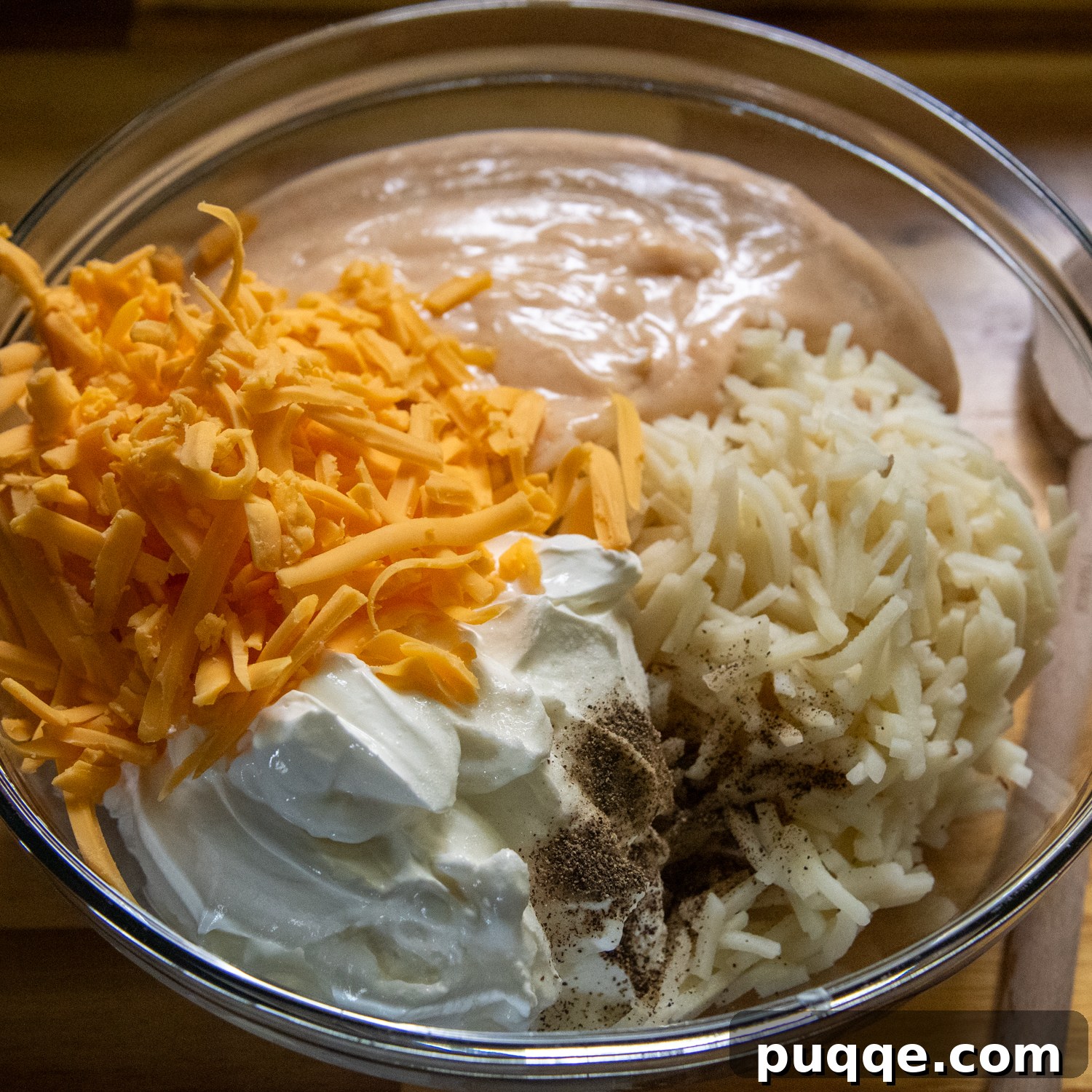 Ultimate Cheesy Gluten-Free Hash Brown Bake from Scratch 5 A large mixing bowl filled with thawed hash browns, shredded cheddar cheese, sour cream, and homemade cream sauce, ready to be combined for the casserole.
