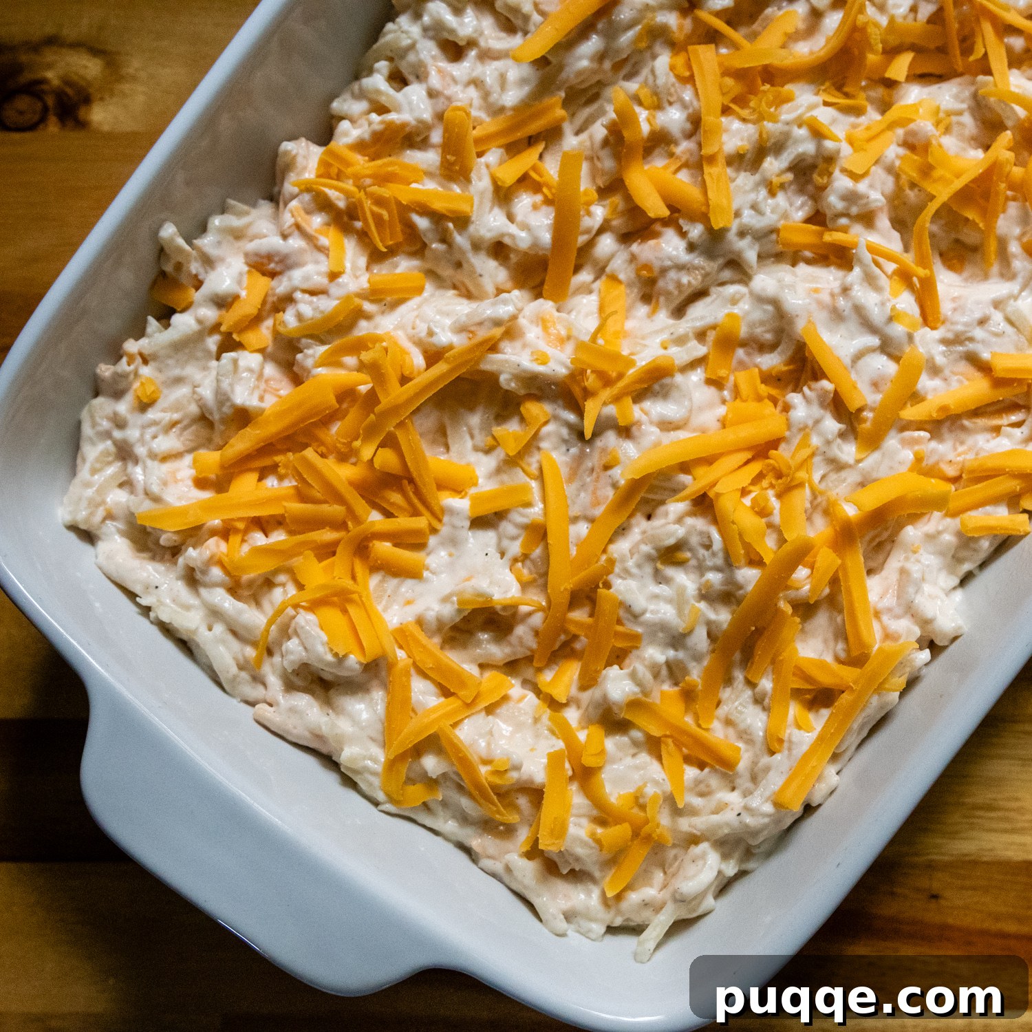 Ultimate Cheesy Gluten-Free Hash Brown Bake from Scratch 6 An uncooked, combined gluten-free hash brown casserole mixture evenly spread in a white 9x13-inch baking dish, topped with additional cheese, ready for the oven.
