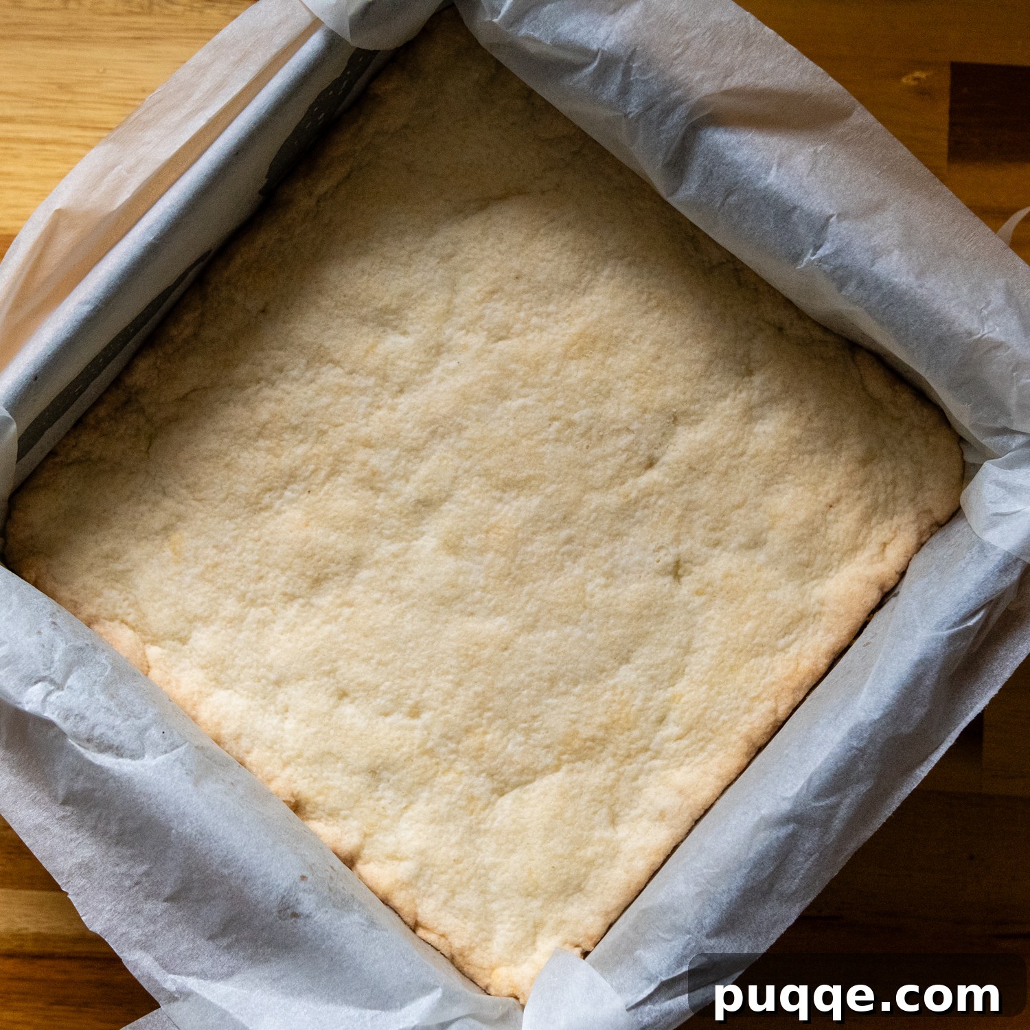 Effortless Gluten-Free Millionaire Bars 6 Baked shortbread layer in a square pan with parchment paper lining.