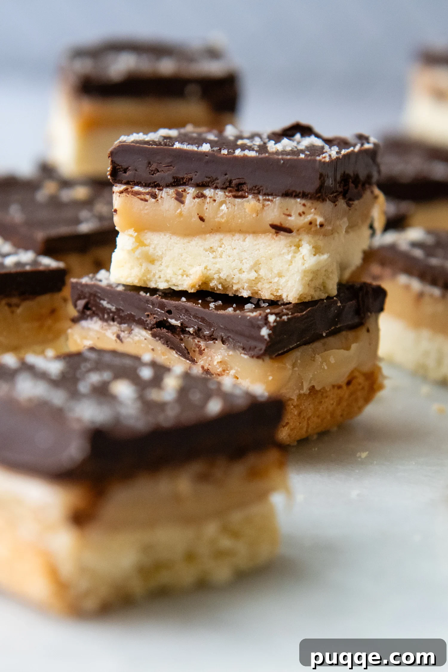 Effortless Gluten-Free Millionaire Bars 9 Cut up bars stacked on top of one another, with the top bar showcasing the distinct layers and a sprinkle of flaky sea salt.