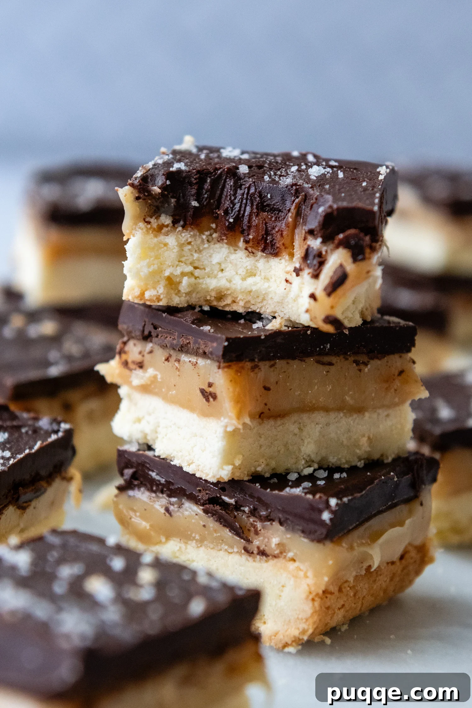 Effortless Gluten-Free Millionaire Bars 10 Stack of bars with the top one having had a bite taken out of it, revealing the layers.