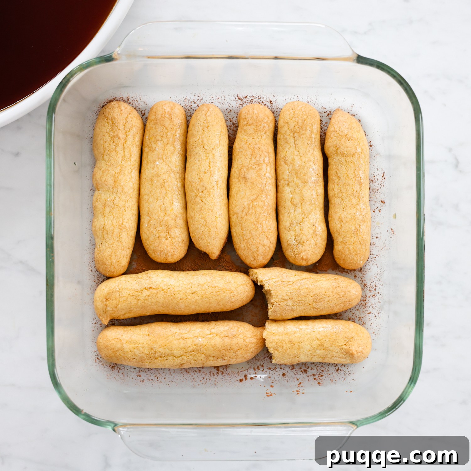 Unforgettable Gluten-Free Tiramisu Made Easy 6 Espresso-dipped gluten-free ladyfingers being arranged in a glass baking dish, forming the first layer of tiramisu.