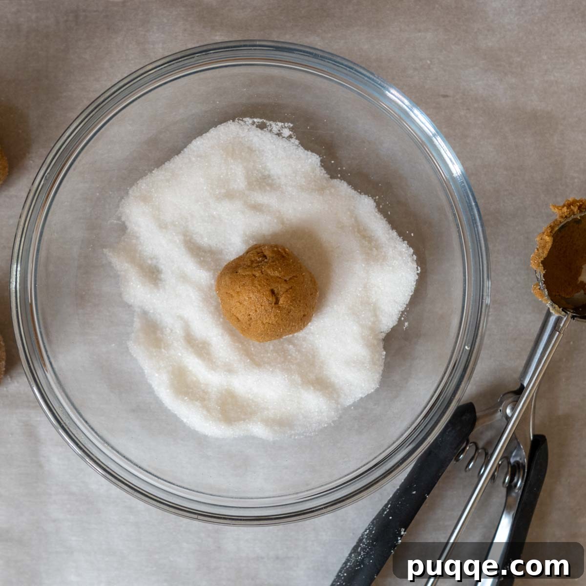 A cookie dough ball being rolled in a bowl of granulated sugar, ready for baking.