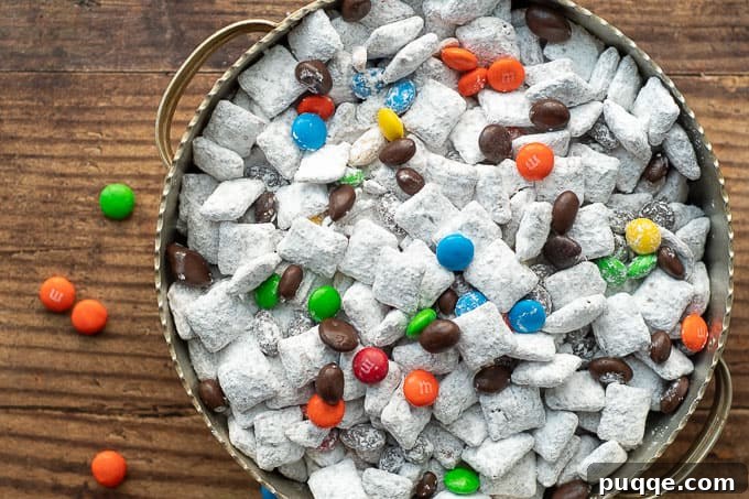 No Bake Nutella Puppy Chow Peanut Butter Free 7 An overhead shot of Nutella Puppy Chow in a silver bowl with M&M's scattered nearby, ready for snacking.