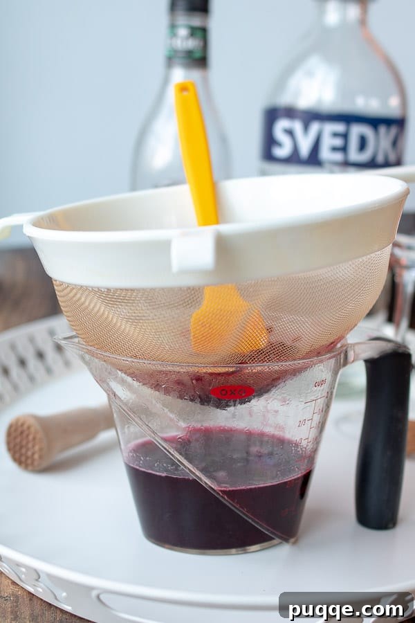 The Ultimate Blackberry Martini 4 A mesh strainer actively mashing fresh blackberries to extract juice for simple syrup.