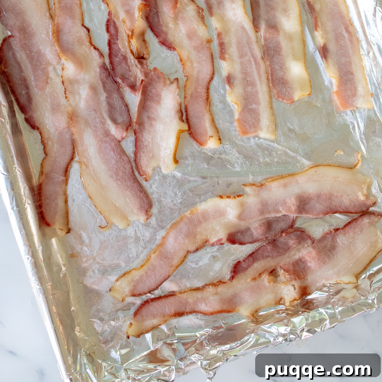 Partially baked bacon strips arranged on a foil-lined baking sheet, golden and slightly crispy.