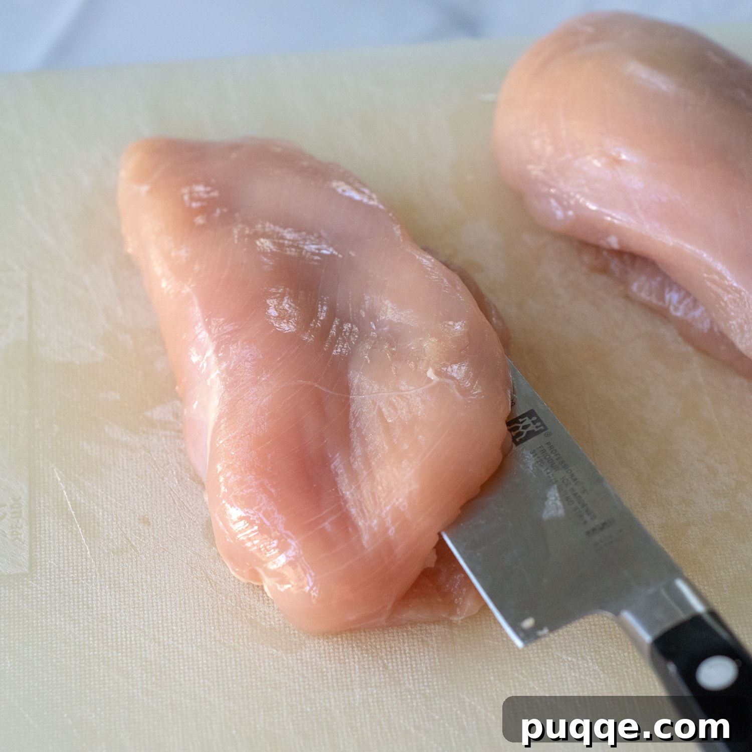 A knife carefully slicing into a raw chicken breast to create a pocket for stuffing.