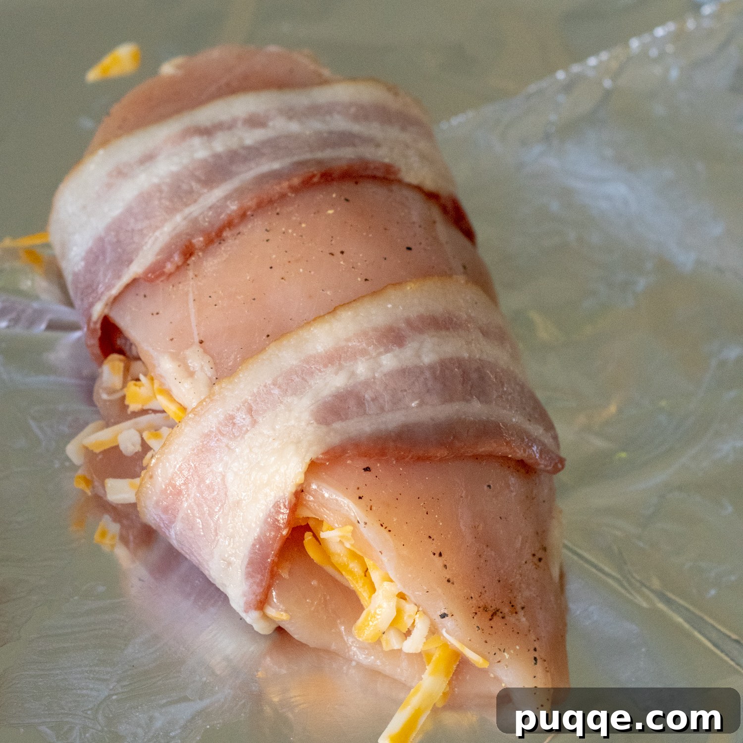 Partially cooked bacon wrapped securely around a cheese-stuffed chicken breast, ready for the oven.