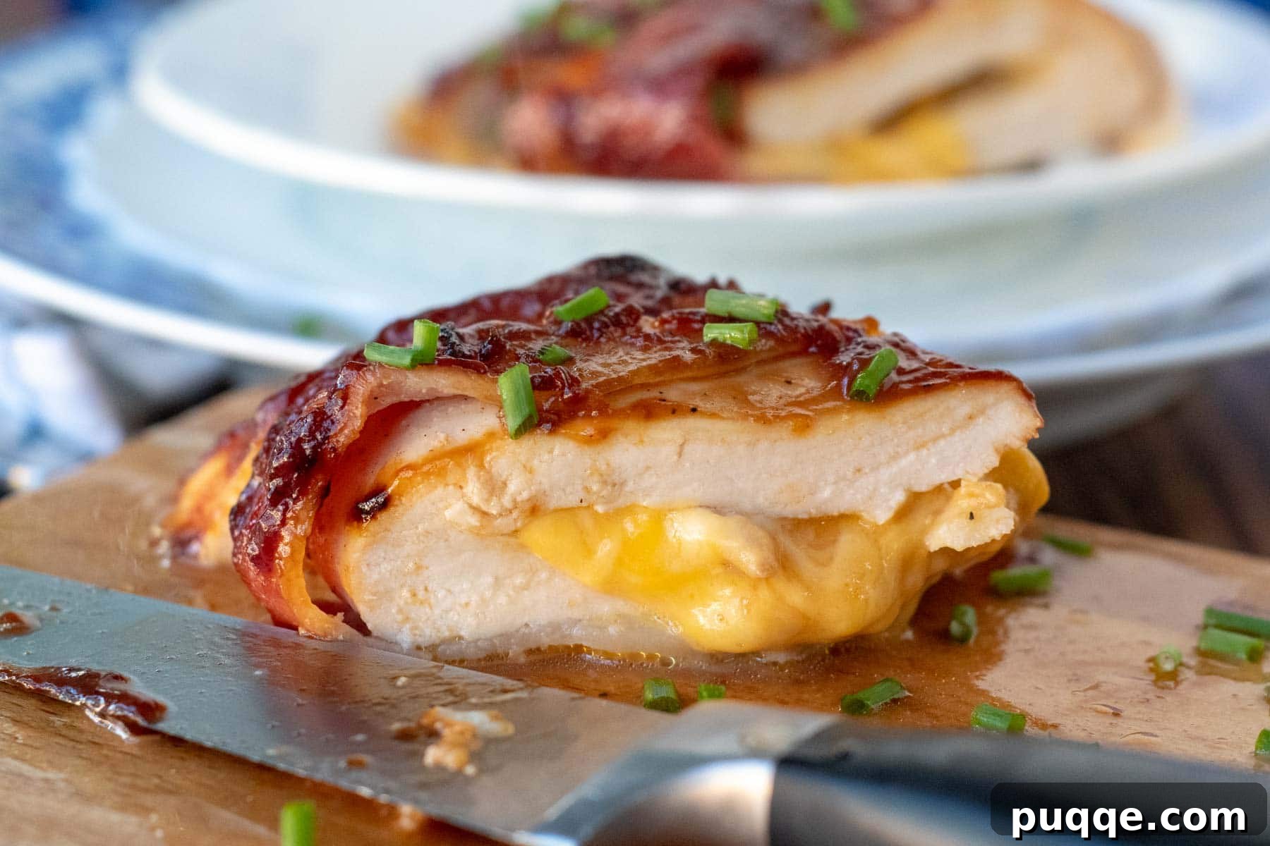 Close-up of a cooked bacon wrapped chicken breast, sliced open to reveal abundant, oozing melted cheese.