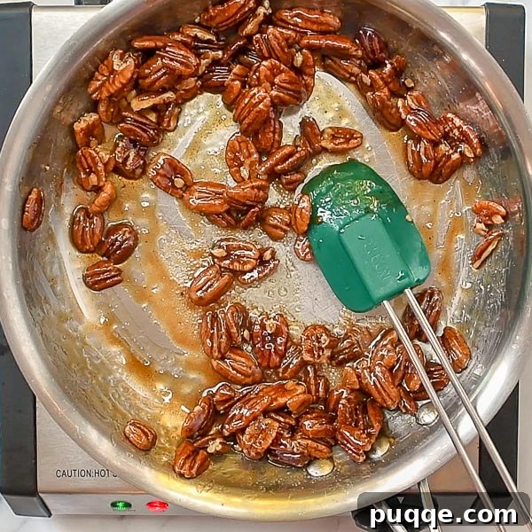 Effortless 5-Minute Candied Pecans 5 The third step of the candied pecan process, showing the syrup thickening and reducing around the nuts in the skillet, creating a perfect glaze.