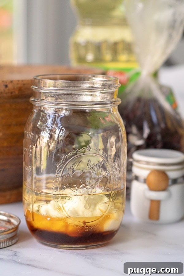 The simple, pantry-staple ingredients for homemade Maple Dijon Vinaigrette gathered in a glass mason jar, ready to be shaken and mixed.
