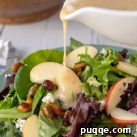 Homemade Maple Dijon Vinaigrette being poured from a white dressing container onto the vibrant Apple Pecan Salad.