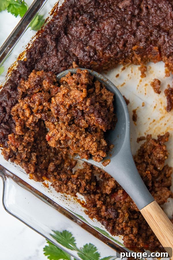 Overhead shot of a spoon scooping up rich, spicy-sweet taco meat from a skillet