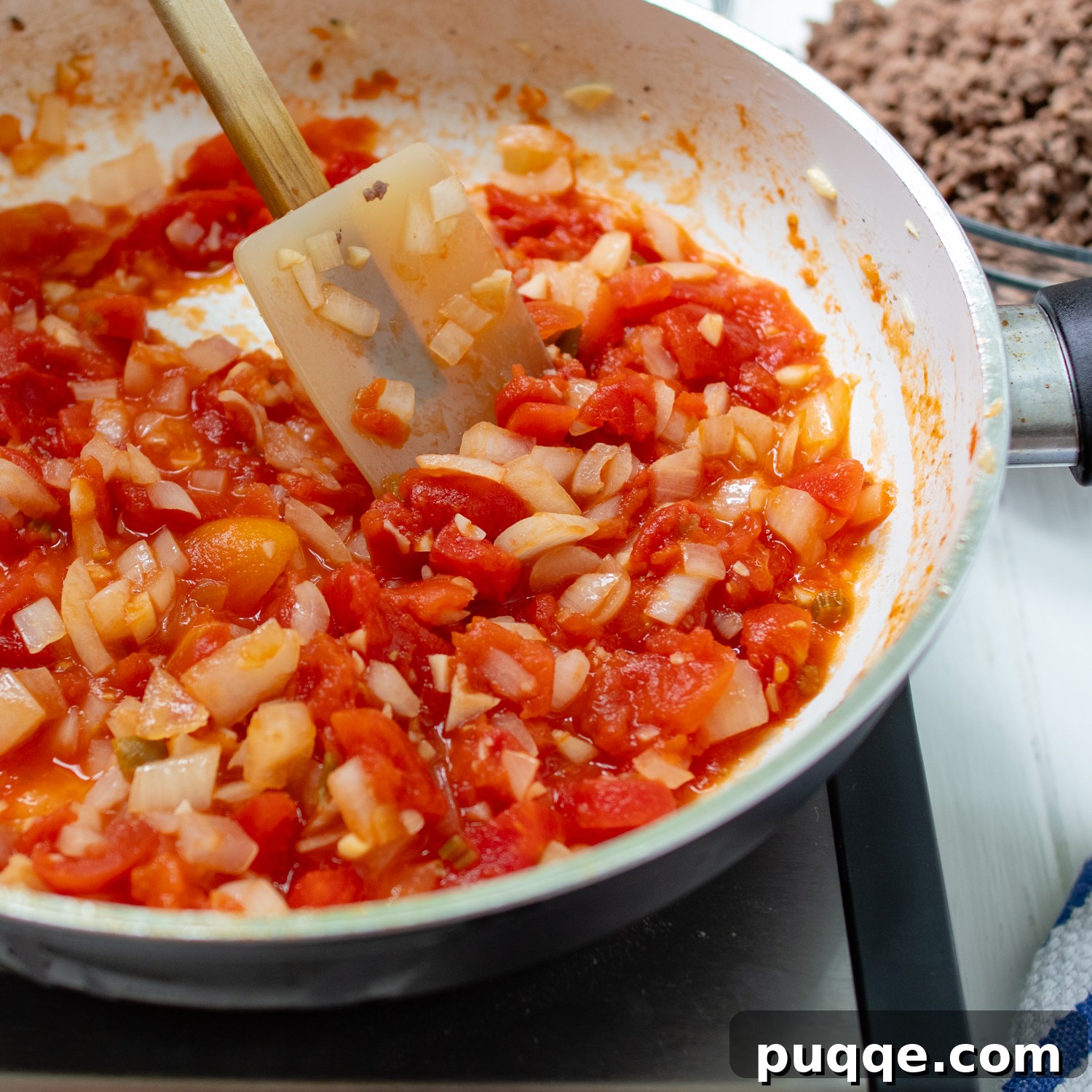 Stewed tomatoes and sautéed onions simmering in a skillet, creating a rich sauce base