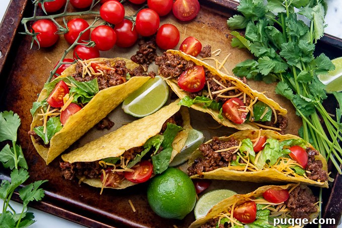 Overhead shot of spicy ground beef tacos with an array of colorful fixings spread on a baking sheet