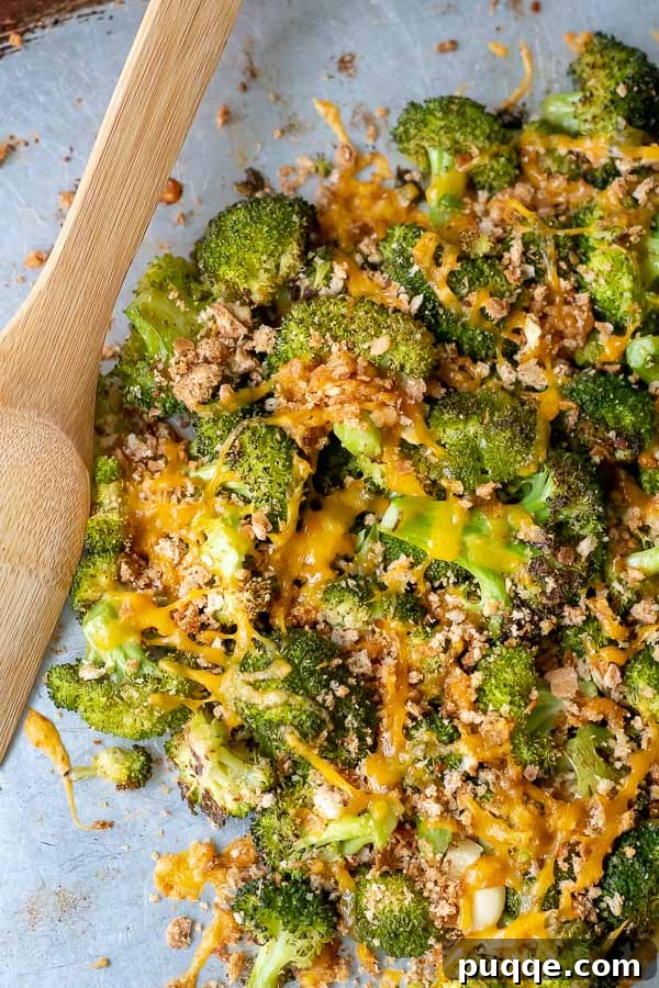 An overhead shot of baked broccoli and cheese in a pile on a baking sheet with a wooden server laying next to it.